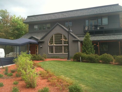 A modern two-story house with large windows, surrounded by green grass and landscaped gardens.