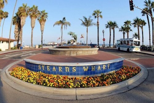 Stearns Wharf entrance with a fountain, colorful flowers, palm trees, and a bus in the background.