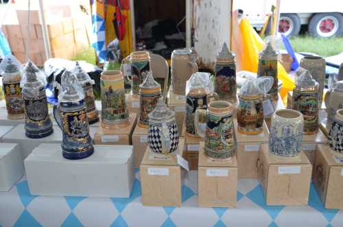 A display of decorative beer steins on a table, featuring various designs and colors, at an outdoor event.