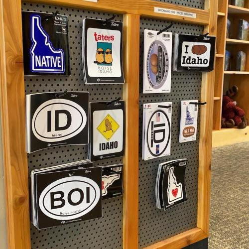A display of various Idaho-themed stickers and magnets on a wooden board, featuring phrases like "Native" and "I Idaho."