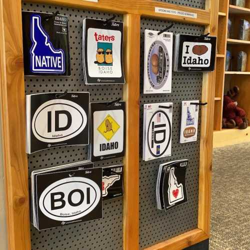 A display of various Idaho-themed stickers and magnets on a wooden board, featuring phrases like "Native" and "I Idaho."