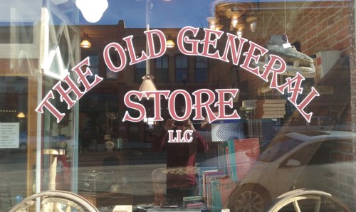 Sign for "The Old General Store LLC" displayed in a shop window, reflecting the street and surroundings.