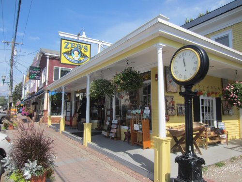 A charming yellow storefront with hanging plants, a clock, and a sign for "Zen's General Store" on a sunny day.