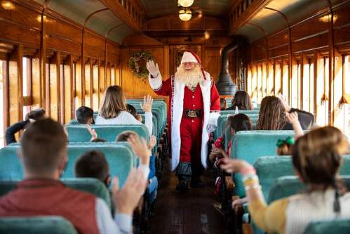 Santa Claus waves to children on a festive train, surrounded by families enjoying the holiday spirit.