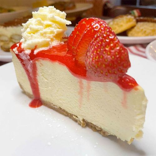 A slice of cheesecake topped with whipped cream and strawberries, drizzled with strawberry sauce on a white plate.