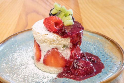 A layered dessert with sponge cake, cream, fresh fruit, and berry sauce, served on a blue plate.