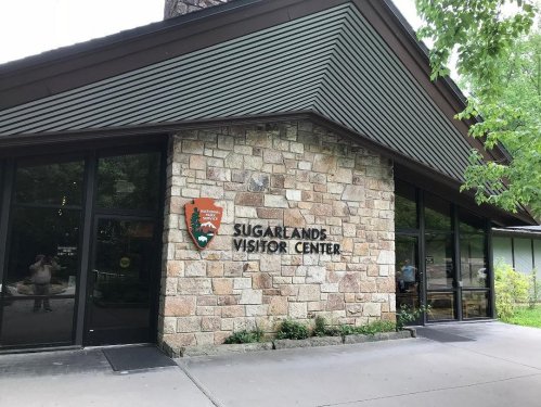 Exterior of the Sugarlands Visitor Center, featuring a stone facade and large windows surrounded by greenery.