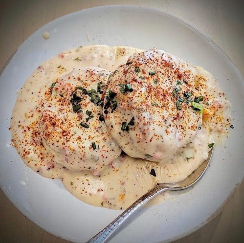 A plate of creamy dumplings topped with herbs and spices, served with a spoon on the side.