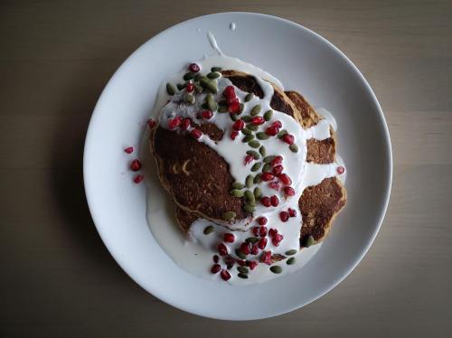 A plate of pancakes topped with yogurt, pomegranate seeds, and pumpkin seeds, arranged artfully.