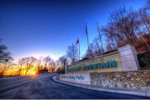 Sign for Lookout Mountain and Ruby Falls at sunset, with trees and flags in the background.
