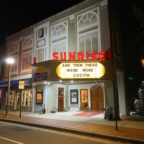 A theater building at night with a marquee displaying "SUNRISE" and "AND THEN THERE WERE NONE 3:00 PM."