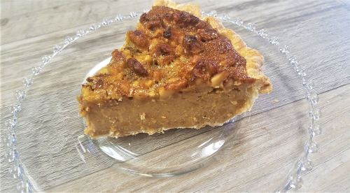 A slice of pie with a golden-brown topping on a clear glass plate, set on a wooden surface.