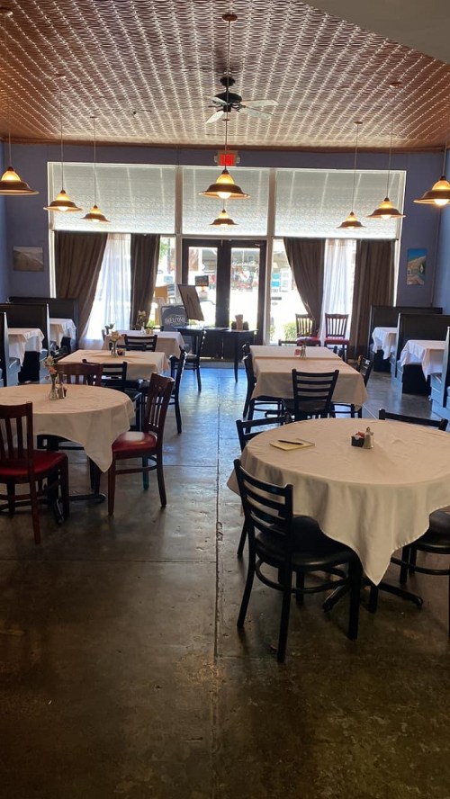 A spacious restaurant interior with tables set for dining, featuring large windows and warm lighting.