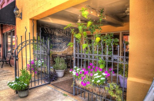 A charming entrance with a wrought iron gate, colorful flowers, and greenery leading to a cozy café.