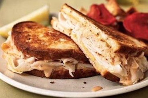 A toasted sandwich filled with turkey and peanut butter, served with potato chips and a lemon wedge on the side.