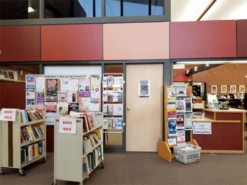 A library interior featuring a bulletin board, book sale carts, and a door leading to another area.