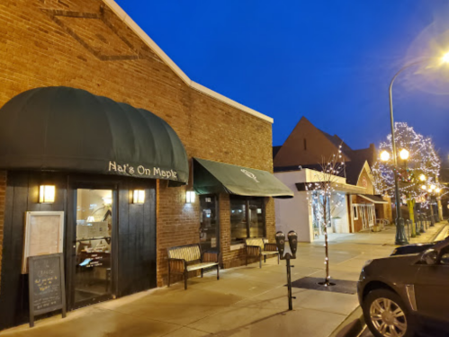 A cozy restaurant with a green awning, surrounded by festive lights on a quiet street at dusk.