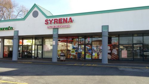 Exterior of Syrena Polish Delicatessen, featuring large windows and a colorful sign, located in a shopping plaza.