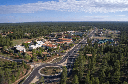 Aerial view of a small town surrounded by dense forest, featuring roads, buildings, and a circular roundabout.
