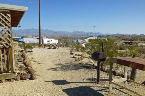 A gravel path leads through a desert landscape with mountains in the background and scattered trailers.