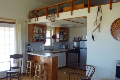 Cozy kitchen and living area with wooden accents, bar stools, and a lofted sleeping space above.