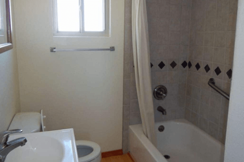 A small bathroom featuring a bathtub with a shower curtain, a toilet, and a sink with a mirror above.