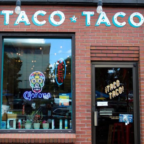 A brick building with a sign reading "Taco Taco" and an open neon sign in the window.