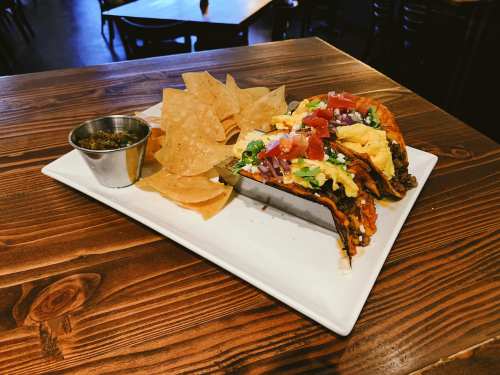 A plate with two tacos filled with toppings, served alongside tortilla chips and a small bowl of salsa.