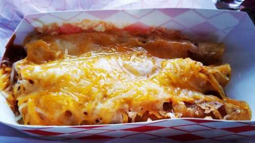 A close-up of a dish featuring two cheesy enchiladas topped with melted cheese in a takeout container.