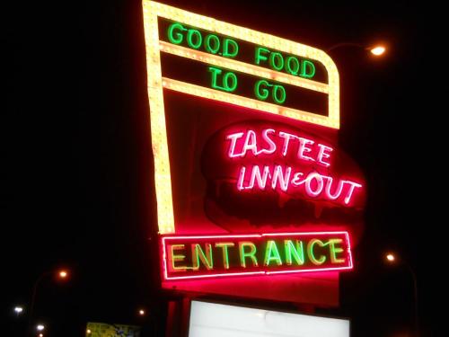Bright neon sign for "Tastee Inn & Out" featuring "Good Food To Go" and "Entrance" illuminated at night.