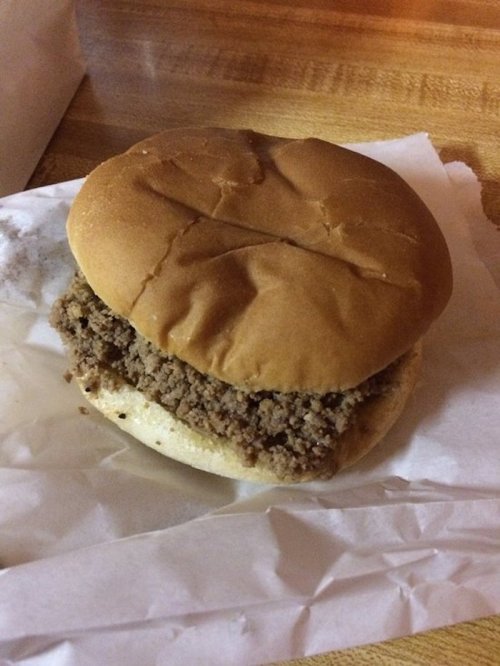 A simple sandwich with a soft bun filled with seasoned ground meat, resting on a piece of white paper.
