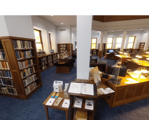 A spacious library interior with wooden shelves, tables, and reading lamps, featuring books and informational displays.
