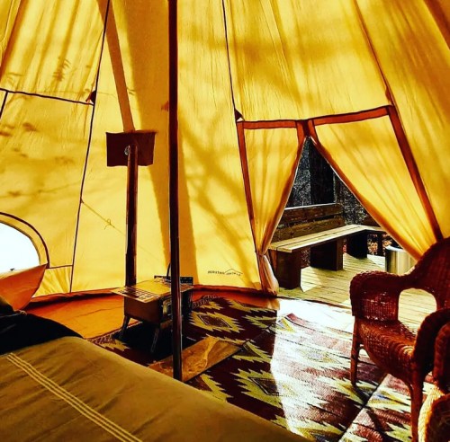 Interior of a cozy tent with warm yellow fabric, a wooden bench outside, and a patterned rug on the floor.