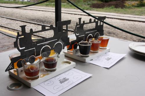 Two flight trays of craft beer shaped like trains, with four small glasses each, set against a railway backdrop.