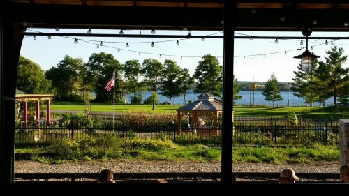 View of a serene lakeside scene with trees, a gazebo, and an American flag, framed by a rustic structure.