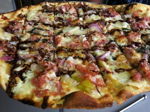 A close-up of a sliced pizza topped with cheese, bacon, onions, and herbs on a crispy crust.