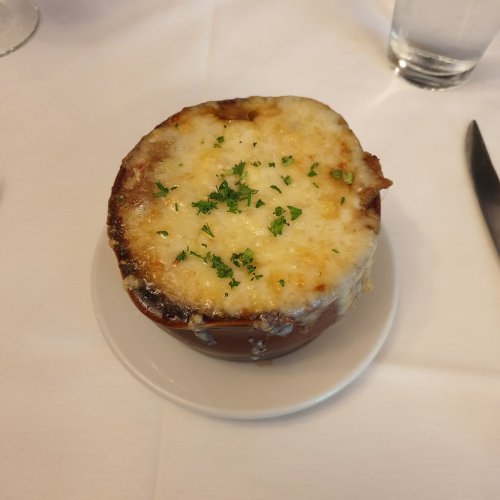 A bowl of French onion soup topped with melted cheese and garnished with parsley, served on a white plate.