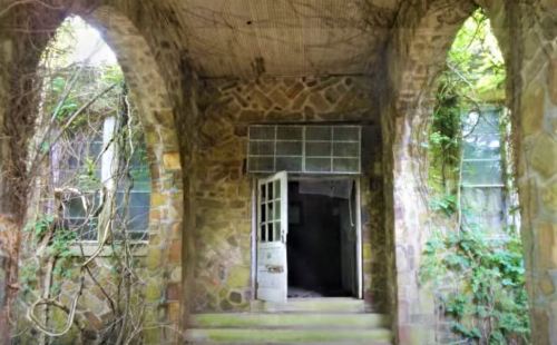 An abandoned stone entrance with overgrown vines and an open door leading into darkness.