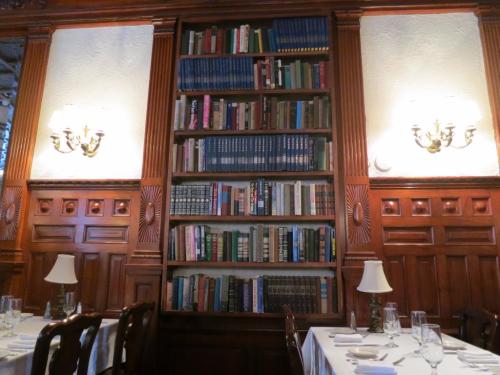 A wooden bookshelf filled with books, flanked by wall sconces, in a cozy restaurant setting.