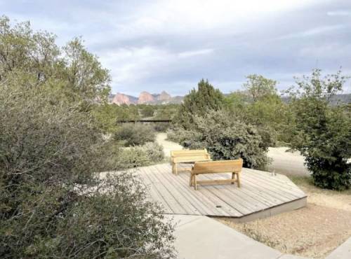 A wooden bench on a platform surrounded by shrubs and trees, with distant rock formations under a cloudy sky.