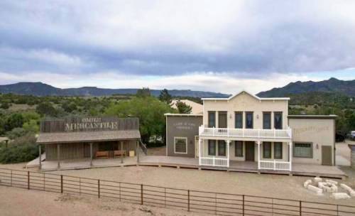 A western-style building complex with a wooden storefront and a two-story structure, set against a mountainous backdrop.