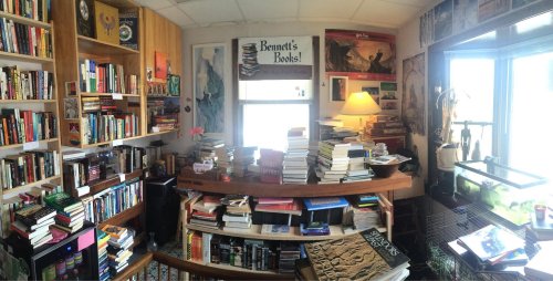 A cozy room filled with bookshelves, stacks of books, and a window, creating a warm reading atmosphere.