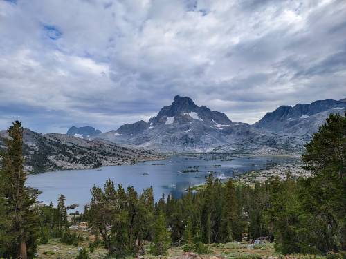 A scenic view of a lake surrounded by mountains and trees under a cloudy sky.