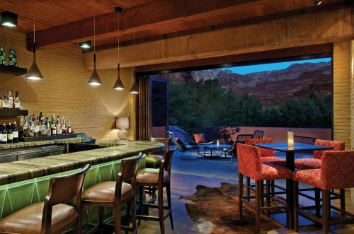 A stylish bar area with wooden beams, a well-stocked bar, and a view of a scenic outdoor patio at dusk.