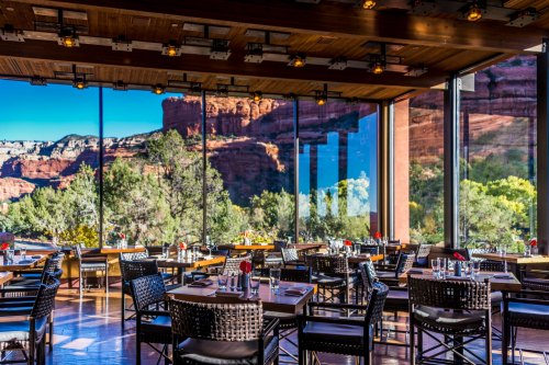 Modern restaurant interior with large windows showcasing a stunning red rock landscape outside.