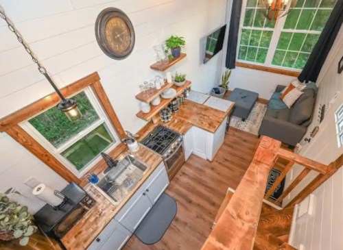 A cozy, modern kitchen with wooden shelves, a clock, and large windows, featuring a stove and seating area.