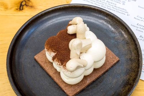 A dessert featuring fluffy white cream topped with cocoa powder, served on a chocolate base, on a black plate.