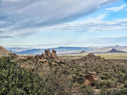 A scenic view of rocky formations and rolling hills under a cloudy sky in a desert landscape.
