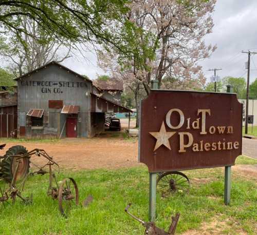 Sign for Old Town Palestine in front of a rustic building with "Gatewood-Shelton Gin Co." written on it.