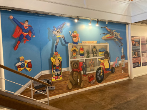 A colorful mural featuring iconic toys and characters, including Superman, a bear, and a vintage toy shelf.